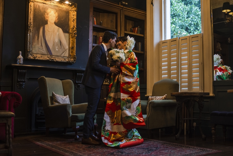 Groom and Bride in vibrant east-asian dress in a small cozy room.